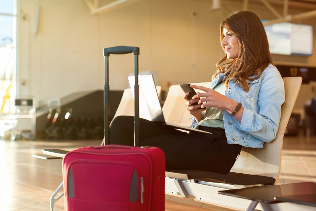 photo of a woman sitting in an airport lounge with a red suitcase