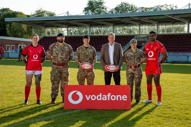 Armed forces staff with rugby players behind Vodafone branded board.